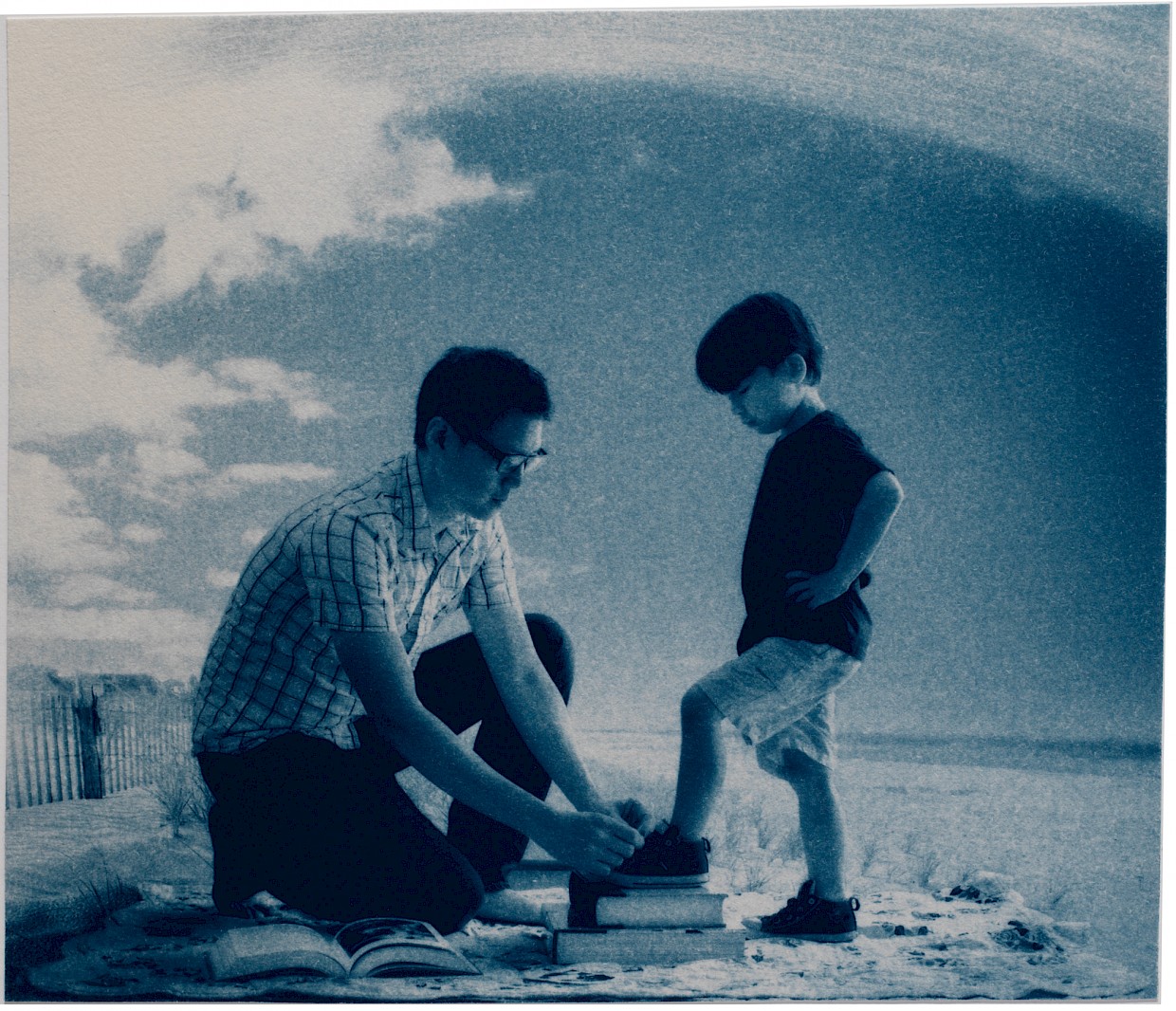 father tying shoes of son on the beach